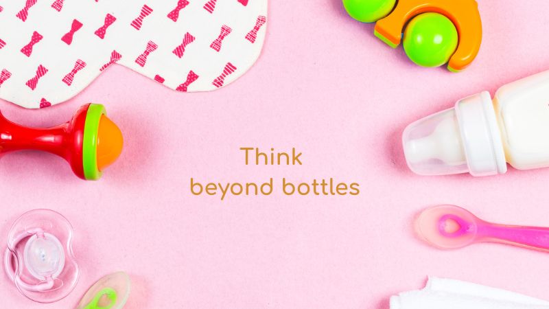 baby care items flat lay with bottles toys and pacifier on pink background